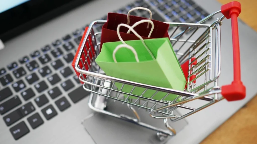 Mini shopping trolley filled with bags on top of a laptop to represent online shopping