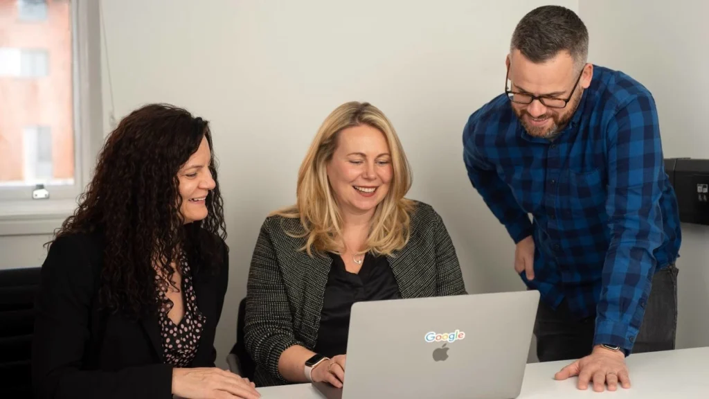 Three members of the Launch team smiling sat around a table looking at a laptop screen.