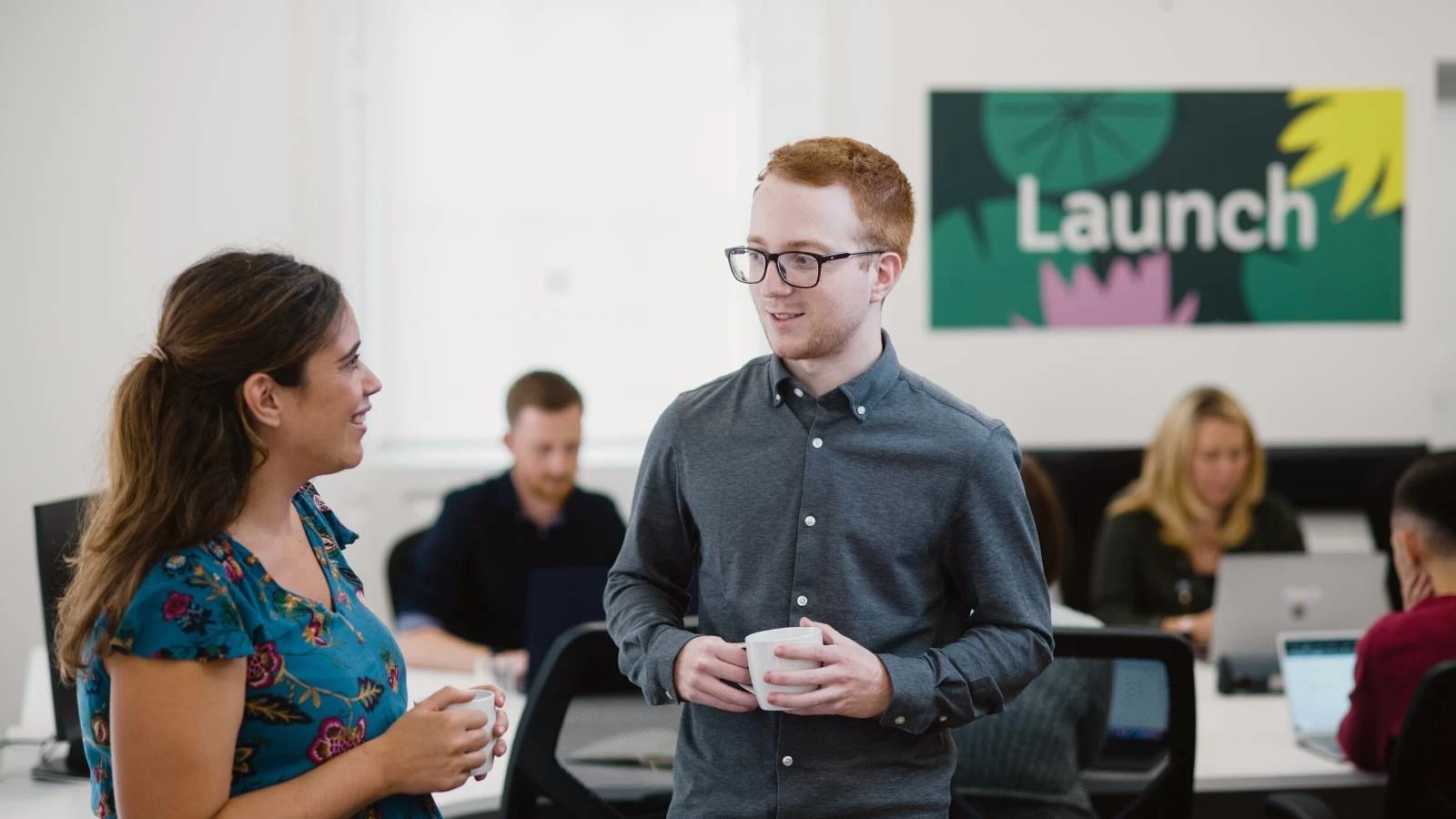 2 members of the Launch team in the office holding coffee mugs and chatting