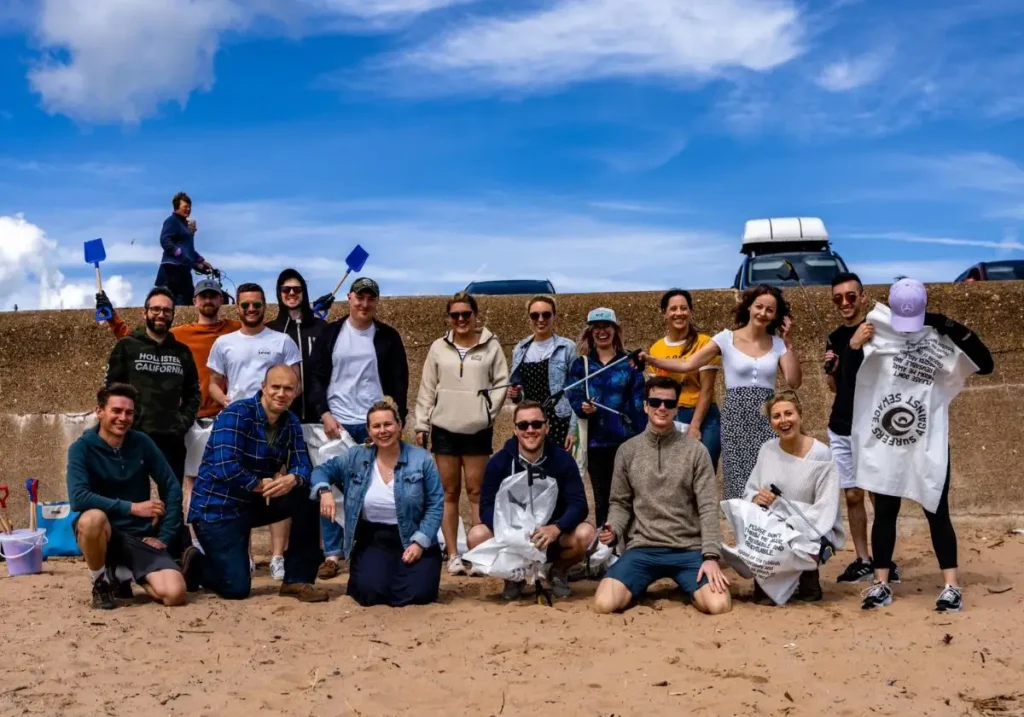 Launch Online Team looking at the camera smiling at the beach holding litter picking equipment for Surfers Against Sewage.