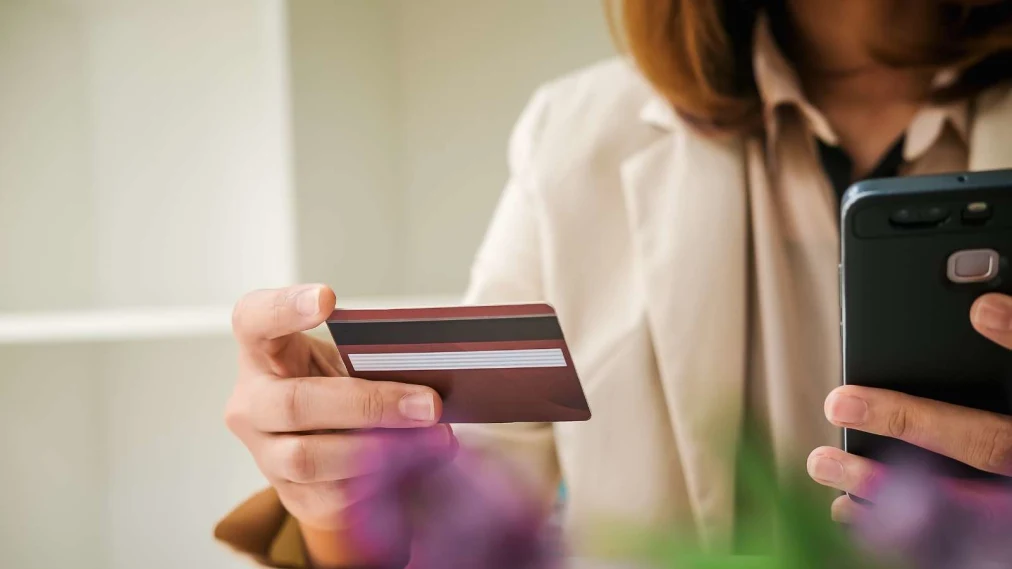 Person sat holding mobile phone in one hand and a credit card in the other.