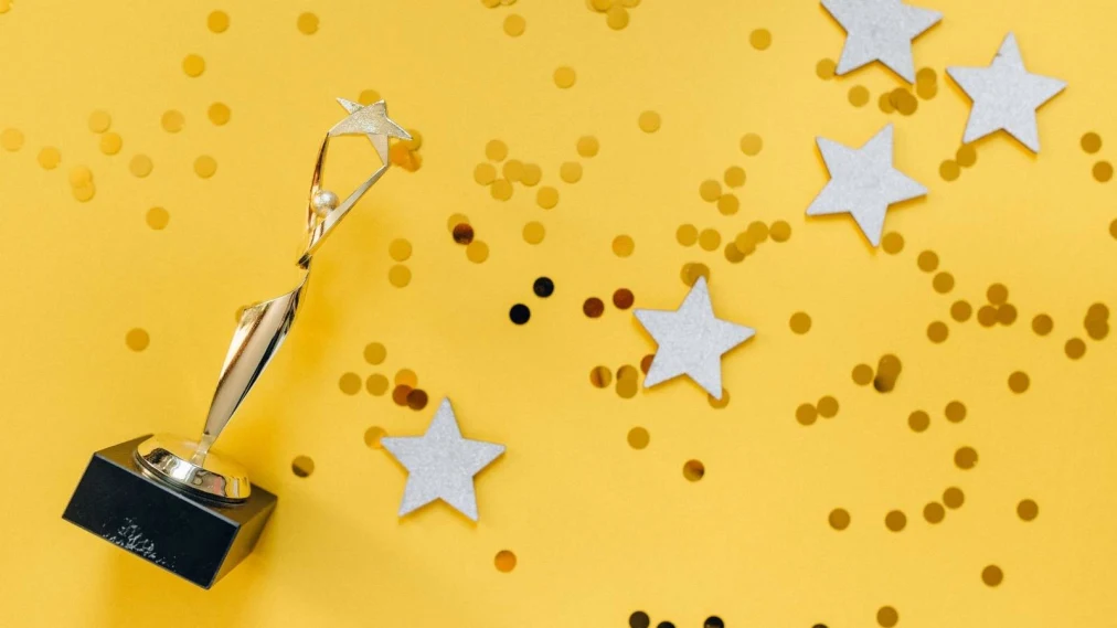 Gold award statue laid on yellow background with stars and gold confetti surrounding.