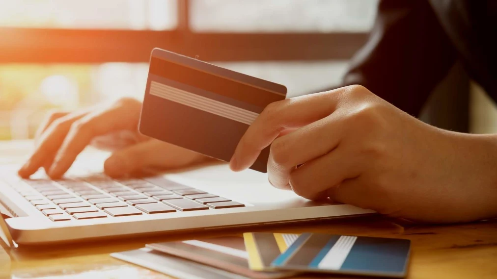 Hand holding a credit card with laptop in background