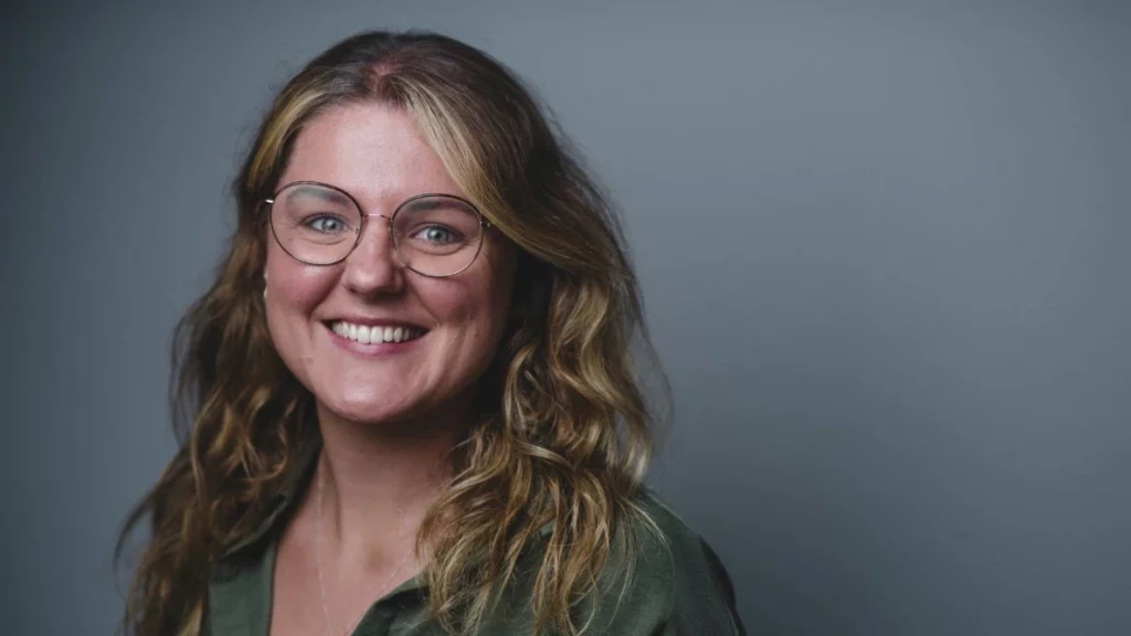 Harriet - Launch Paid media Director. Young Woman Smiling with glasses and curly blonde brown hair.