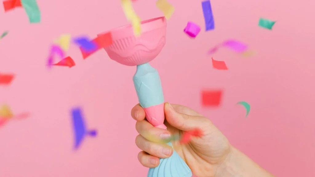 Hand holding a blue and pink trophy on a pink background with confetti