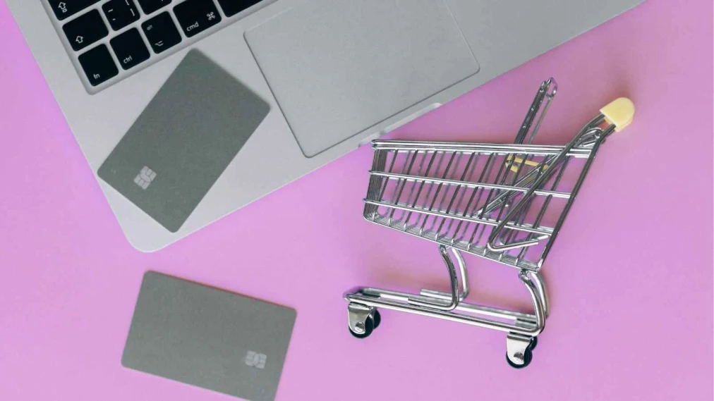 Mini shopping cart with credit cards next to a laptop