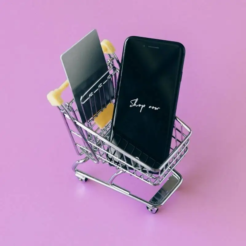 Pink background with mini shopping trolley holding a mobile phone and credit card