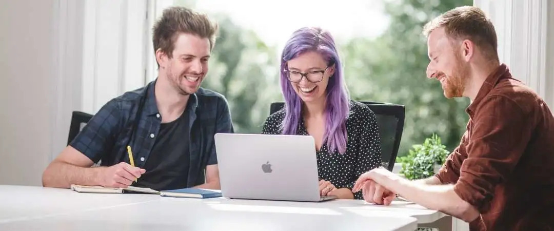 Three people sat looking at a laptop screen smiling.