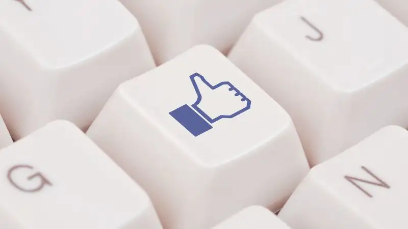 Close up image of a white keyboard button displaying a blue facebook Thumbs Up Icon