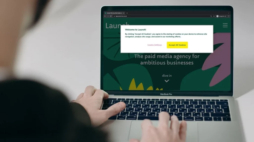 Laptop screen with blurred person in foreground. Laptop shows Launch new website with cookie policy popup