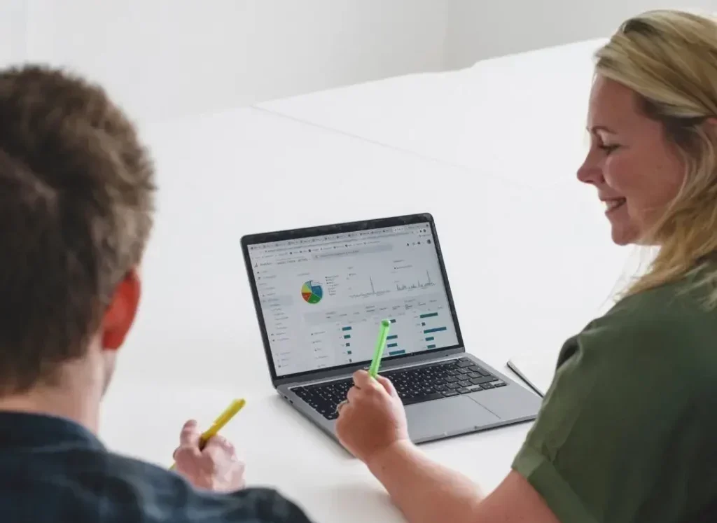 Back shot of woman and man sat at a table looking at Google analytics on a laptop screen.