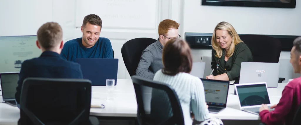 Launch team all sat around a large white desk, talking and looking at laptop screens