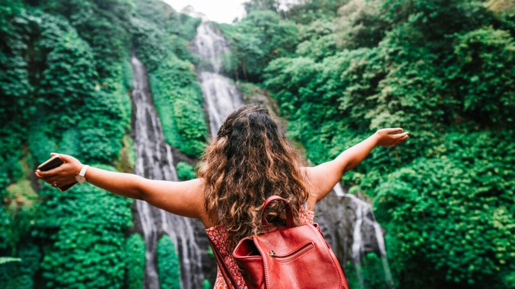 A woman faces a waterfall with open arms