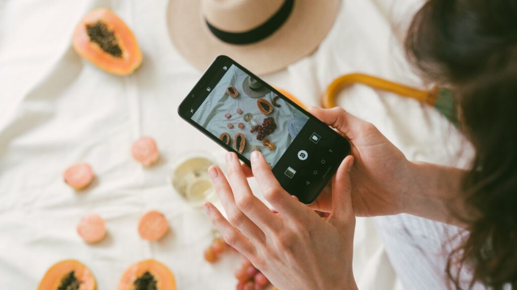 A woman uses a smartphone to snap a picture of a flatlay of fruit