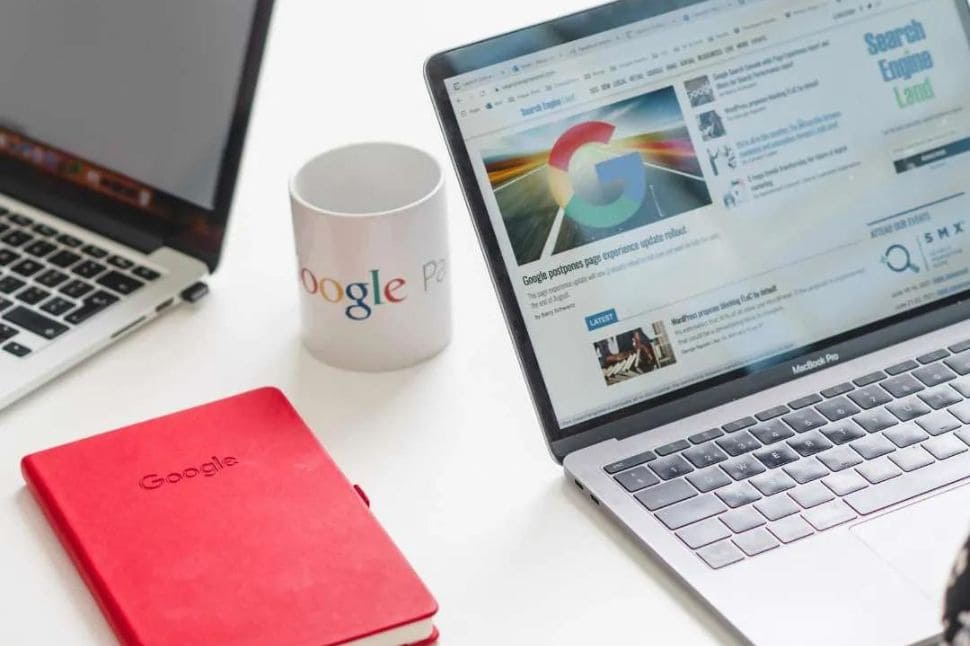 Desk with a Google mug, red notebook and laptops showing Google on the screens