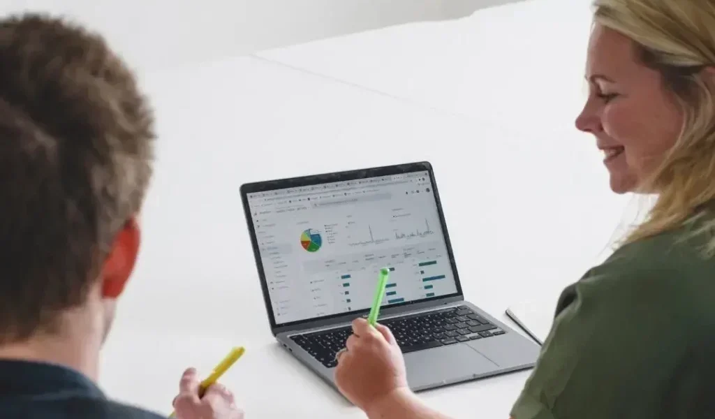 Back shot of woman and man sat at a table looking at Google analytics on a laptop screen.