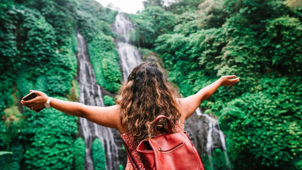 A woman faces a waterfall with open arms